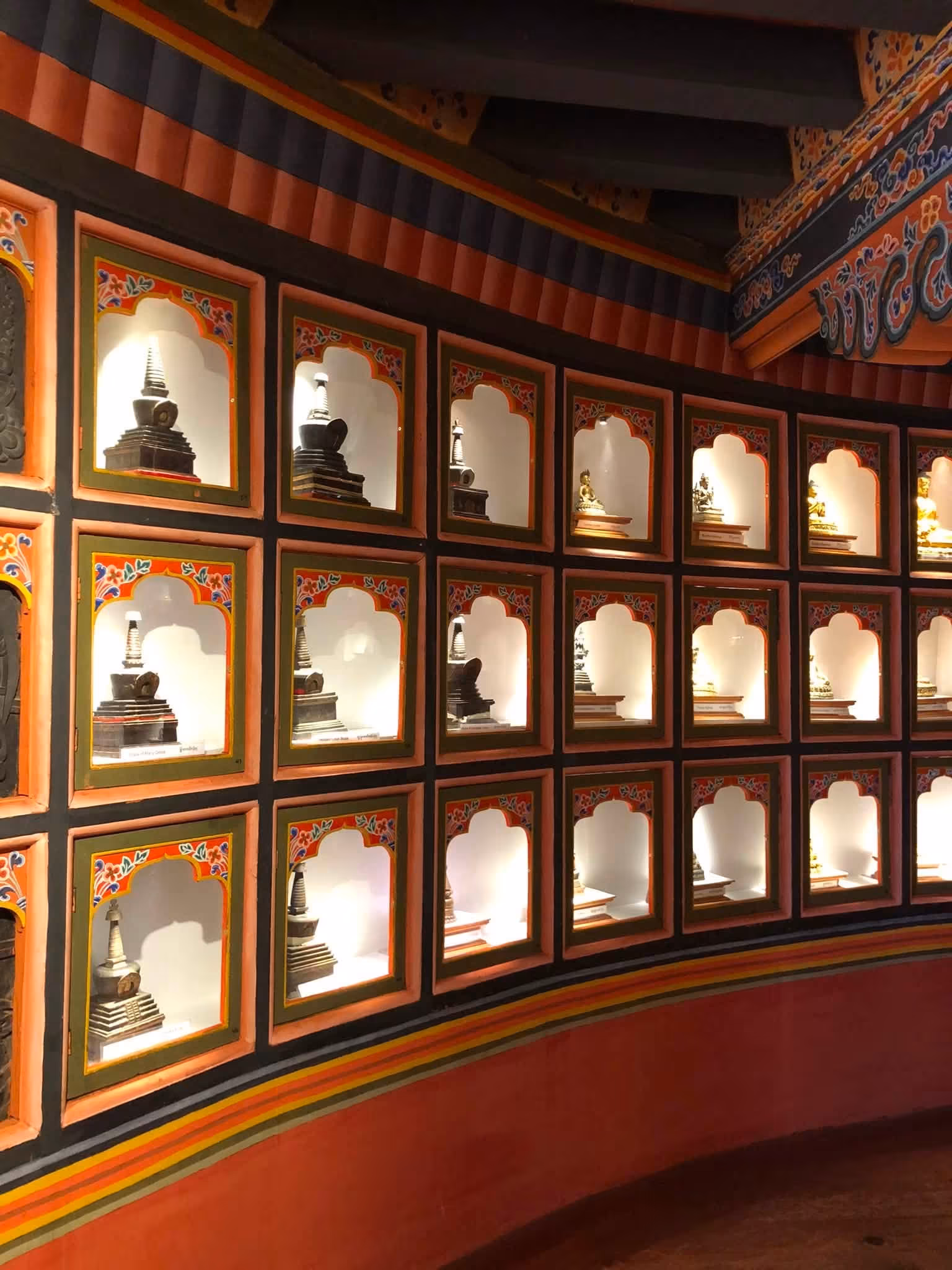 A curved wall of lit niches holding small statues and stupas