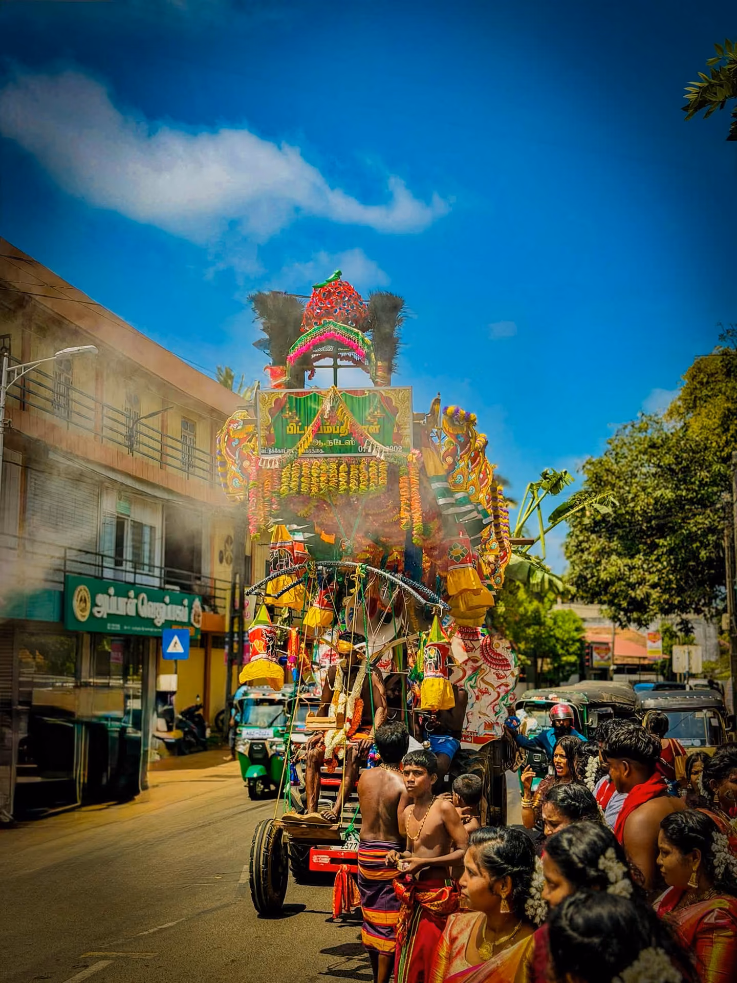 A decorated temple chariot drawn through the street with devotees alongside