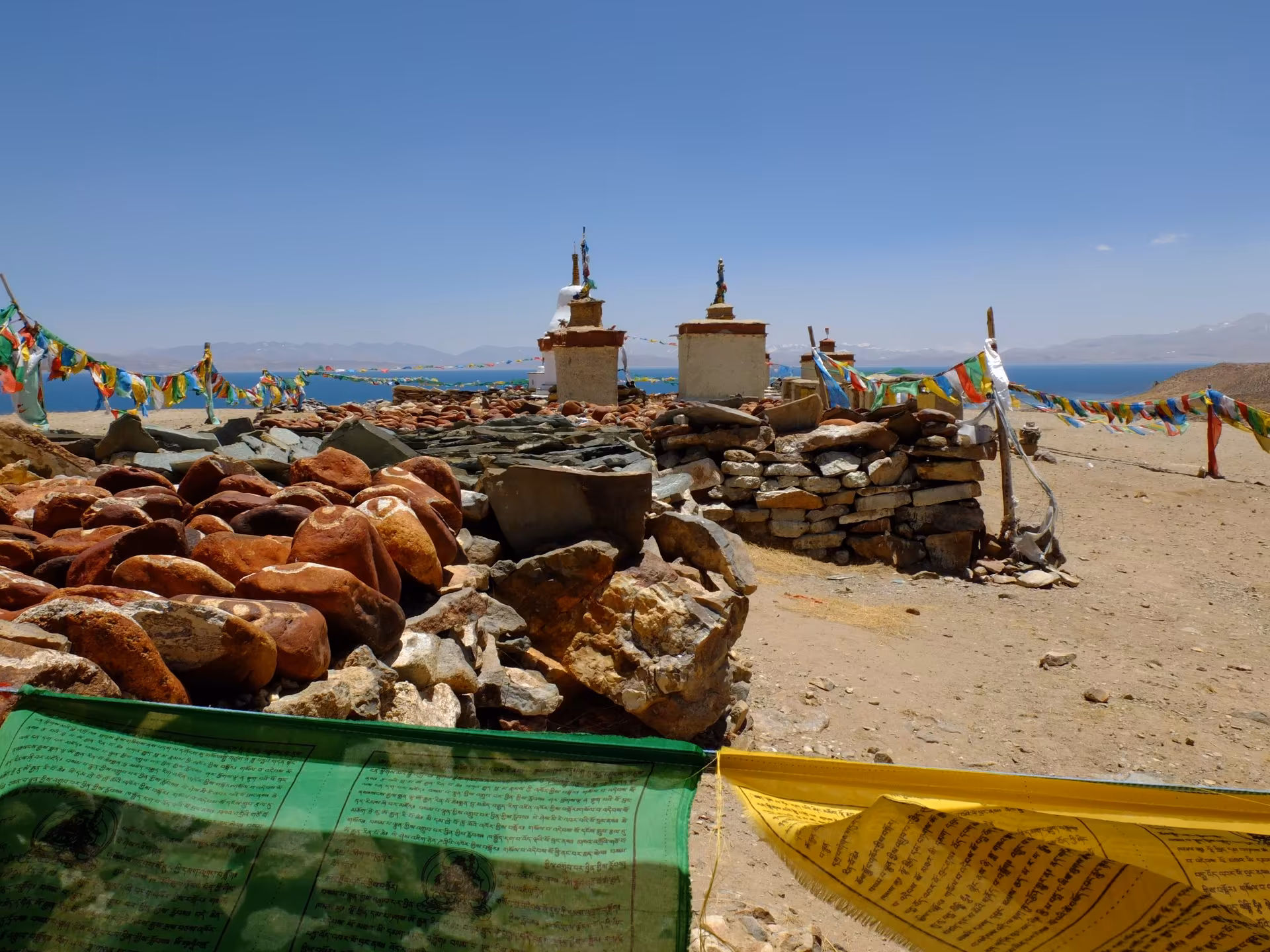 Mani stones, small chortens and prayer flags on the shore below Chiu Gompa, with Manasarovar behind