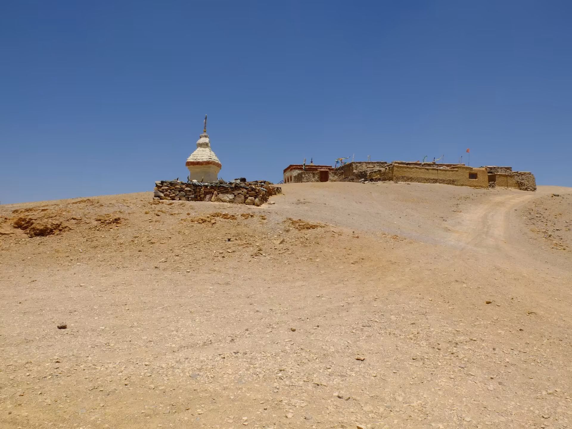 A white chorten and low monastery buildings on a bare ridge under a cloudless sky