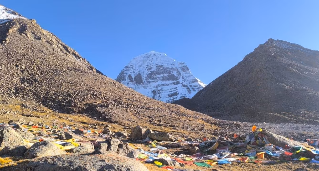 Mount Kailash's distinctive snow dome framed between two dark ridges above scattered prayer flags