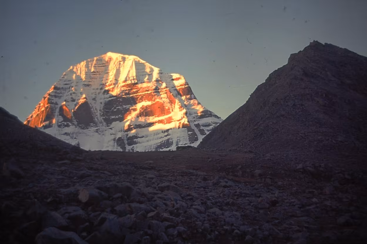 Mount Kailash lit red and gold by the setting sun, framed between dark foreground slopes